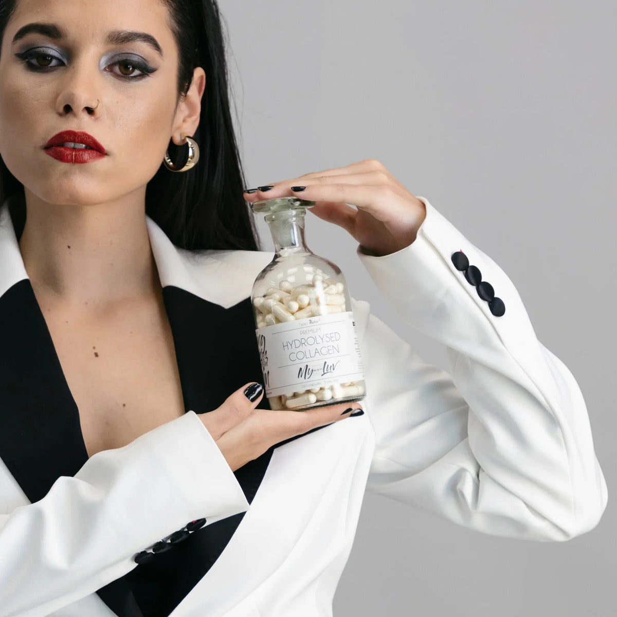 A woman hold up a glass supplement bottle with the label Peptan® Premium Hydrolysed Collagen Capsules by My Beauty Luv